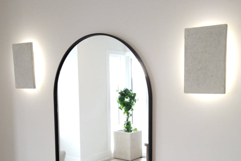 Arched mirror on a white wall with two square light fixtures.