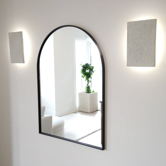 Arched mirror on a white wall with two square light fixtures.